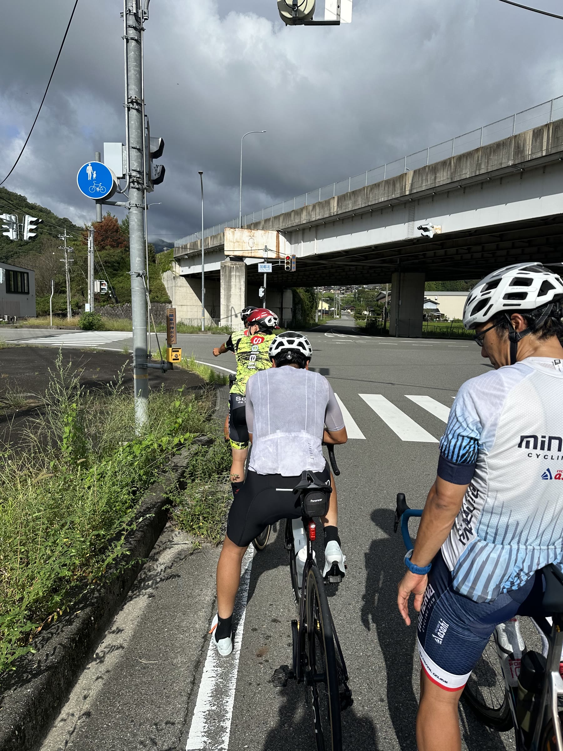 曇り空の交差点で、走り出すのを待つ3人のロードバイクライダー